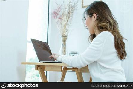 A woman wearing casual dress, using laptop for work or online shopping while staying in bedroom at home. Lifestyle and Technology Concept.