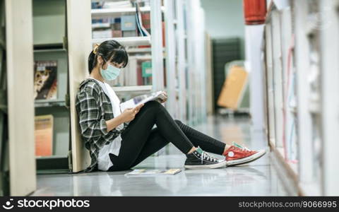 A woman wearing masks is sitting reading a book in the library.