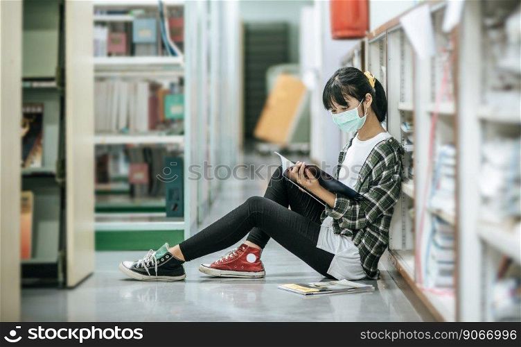 A woman wearing masks is sitting reading a book in the library.