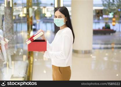 A woman wearing protective mask holding a gift box in shopping mall, shopping under Covid-19 pandemic, thanksgiving and Christmas concept.. Woman wearing protective mask holding a gift box in shopping mall, shopping under Covid-19 pandemic, thanksgiving and Christmas concept.