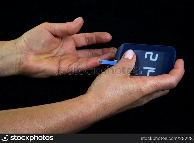 A woman with advanced diabetes measuring blood glucose level using a glucometer. Clearly visible a drop of blood on a strip measuring time and black dots on the fingers, traces of long-thrusting fingers glucometer. Isolated on black. Horizontal view.
