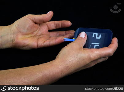 A woman with advanced diabetes measuring blood glucose level using a glucometer. Clearly visible a drop of blood on a strip measuring time and black dots on the fingers, traces of long-thrusting fingers glucometer. Isolated on black. Horizontal view.