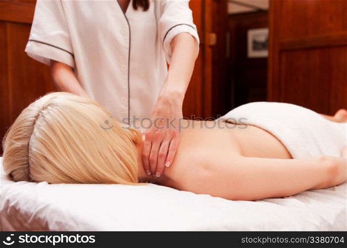 A woman with arms down receiving a shoulder massage in a retro styled spa