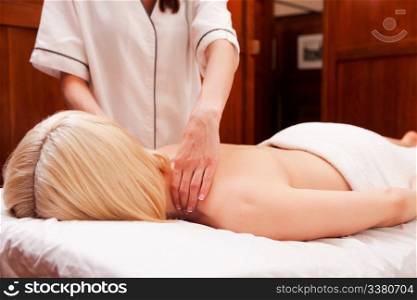 A woman with arms down receiving a shoulder massage in a retro styled spa