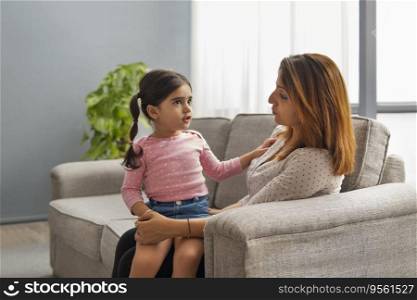 A WOMAN WITH HER DAUGHTER ON LAP SITTING IN SOFA AND TALKING TO CHILD