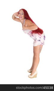 A woman with long red hear wearing a dress and heels bendingforwards, isolated for white background.