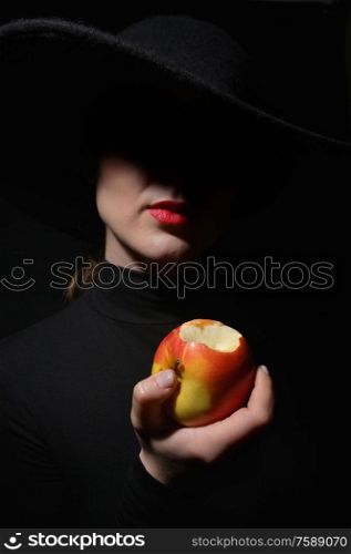 A Woman With Red Lips In A Black Hat holding bitten apple