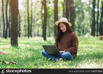 A woman working and typing on laptop keyboard while sitting in the park