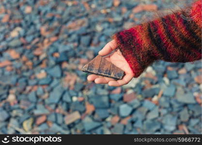 A womans hand is holding a piece of slate outside with gravel and rubble on the ground