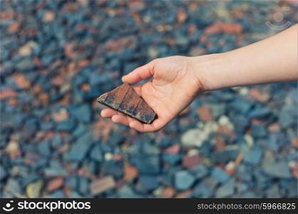 A womans hand is holding a piece of slate outside with gravel and rubble on the ground