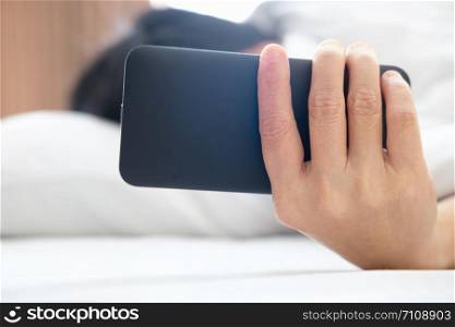 A women are playing phone on a white bed in the morning after waking up.