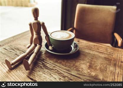 a wood man sitting and touch the hot mocha coffee or capuchino in the green cup on the wooden table