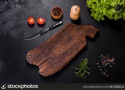 A wooden cutting board with a kitchen knife with sπces and herbs on a dark concrete background. Cooking at home. A wooden cutting board with a kitchen knife with sπces and herbs