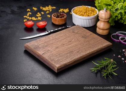 A wooden cutting board with a kitchen knife with sπces and herbs on a dark concrete background. Cooking at home. A wooden cutting board with a kitchen knife with sπces and herbs