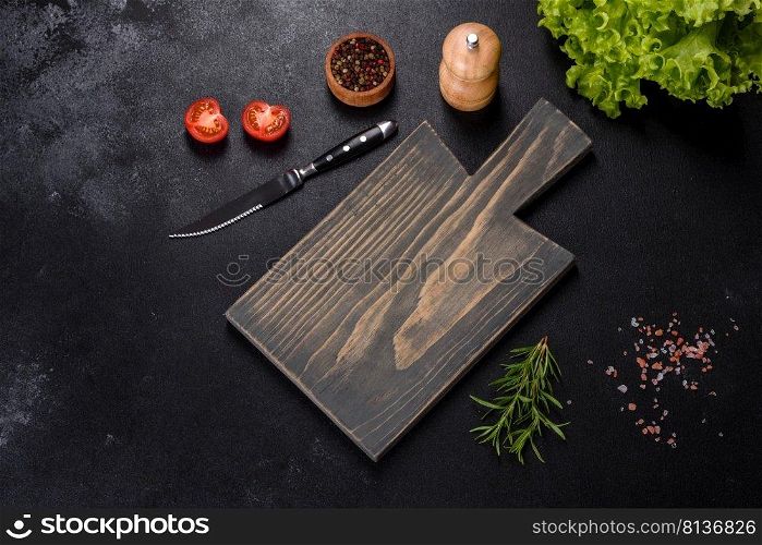 A wooden cutting board with a kitchen knife with spices and herbs on a dark concrete background. Cooking at home. A wooden cutting board with a kitchen knife with spices and herbs