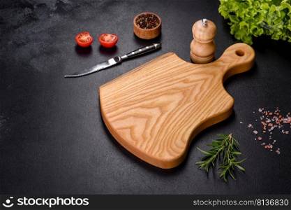 A wooden cutting board with a kitchen knife with spices and herbs on a dark concrete background. Cooking at home. A wooden cutting board with a kitchen knife with spices and herbs