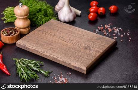A wooden cutting board with spices, herbs, cherry tomatoes and salt on a black concrete background. Cooking at home. A wooden cutting board with spices, herbs, cherry tomatoes and salt on a black concrete background