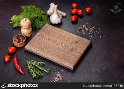 A wooden cutting board with spices, herbs, cherry tomatoes and salt on a black concrete background. Cooking at home. A wooden cutting board with spices, herbs, cherry tomatoes and salt on a black concrete background