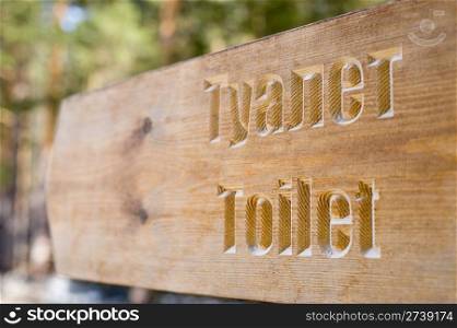 a wooden direction sign of toilet in English and Russian