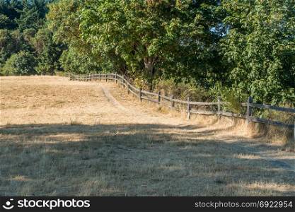 A wooden fence separates a dry field from lush green trees.