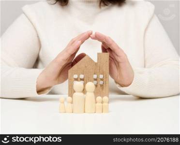 a wooden house and figures of a family, two female palms protect objects from above. Real estate insurance concept, happy family