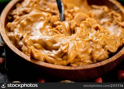 A wooden plate of peanut butter with a spoon. Macro background. High quality photo. A wooden plate of peanut butter with a spoon.