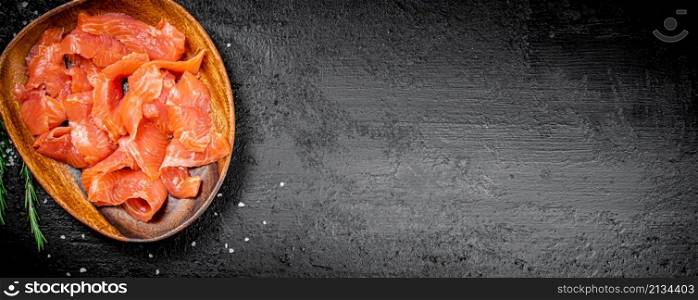 A wooden plate with slices of salted salmon. On a black background. High quality photo. A wooden plate with slices of salted salmon.