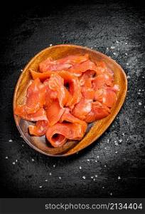 A wooden plate with slices of salted salmon. On a black background. High quality photo. A wooden plate with slices of salted salmon.