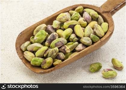 a wooden scoop od raw pistachio nuts on a rough white painted barn wood background