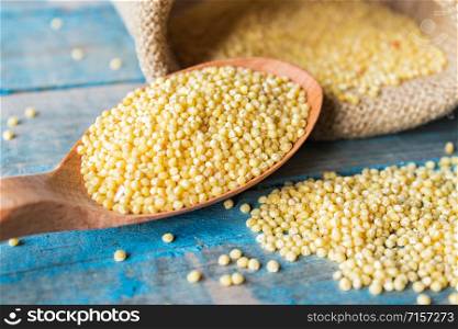 A wooden spoon with millet lies near a bag of millet against the background of old blue boards. Close-up.. A wooden spoon with millet lies near a bag of millet against the background of old blue boards.