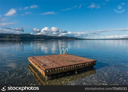 A wooden swim float sits on Hood Canal in Washington State. Blue cloudy skies are reflected in calm waters.