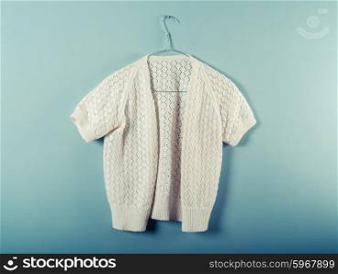 A woolen jumper is hanging on a wire hanger against a blue wall