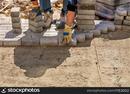 A worker lays paving slabs on a bright sunny day on a prepared smooth sand base on the pavement, image with copy space.. A worker lays paving slabs on a prepared flat sandy platform on the sidewalk on a bright sunny day.