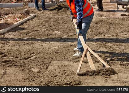 A worker levels the sand base with a wooden level to begin laying paving slabs in the pedestrian area of a city street, image with copy space.. A worker levels the sand foundation with a wooden level for subsequent laying of tiles on the sidewalk.