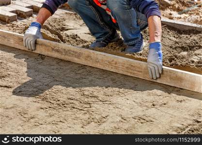 A worker levels the sand foundation with a wooden level to continue laying paving slabs, image with copy space, image with copy space.. The worker cleans and levels the sand base with a wooden board for subsequent smooth laying of tiles on the sidewalk.