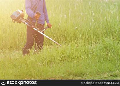 A working man mowing grass in the garden with gasoline brush cutter.