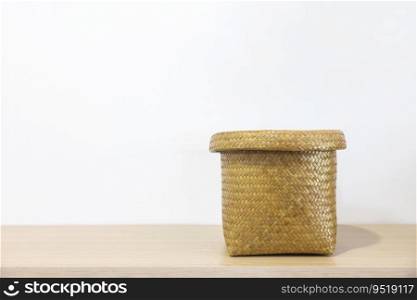 A woven basket lies on a wooden table against a white wall. Handmade basket. Thailand&rsquo;s native handicrafts.