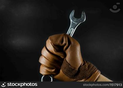 a wrench was holding by leather glove man hand in dark light