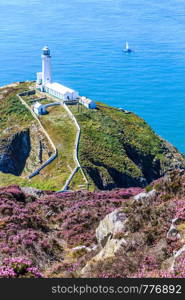 A yacht sails past the North Stack lighthouse, Anglesey, North Wales, United Kingdom