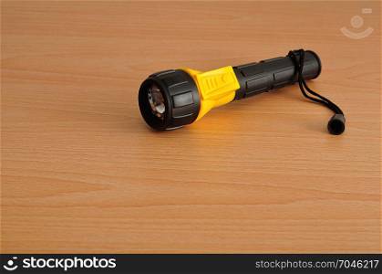 A yellow and blue plastic flashlight isolated against a wooden background