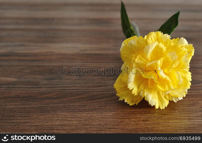 A yellow artificial carnation on a wooden background