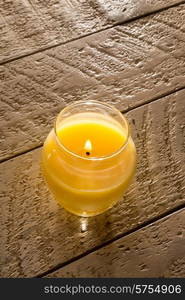 A yellow citronella candle in a glass jar. the candle is lid and standing on a white washed wooden table.