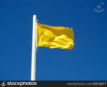 A yellow flag on the blue sky blowing in the wind