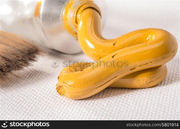 A Yellow Ochre oil paint paste is pressed from a tube on to a white canvas.
