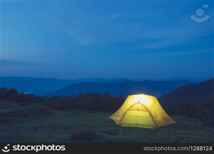 A yellow tent in mountains. Camping under night sky