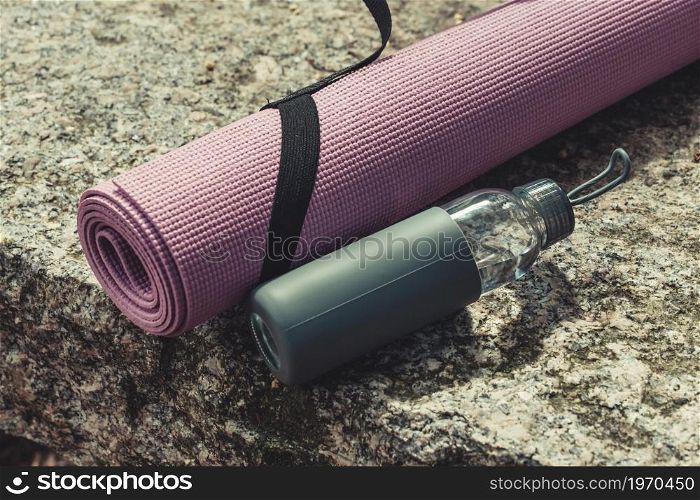 A yoga mat and a bottle of water resting over a rock with copy space