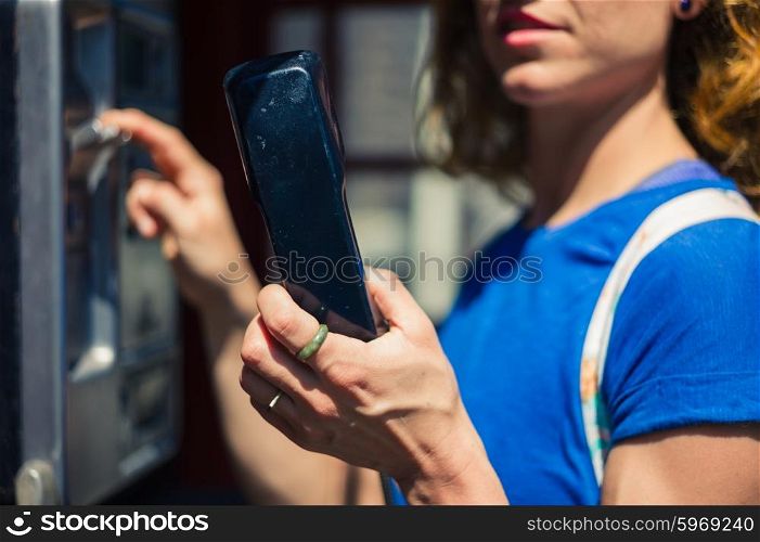 A yooung woman is using a public telephone in the city on a sunny summer day