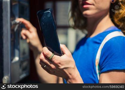 A yooung woman is using a public telephone in the city on a sunny summer day
