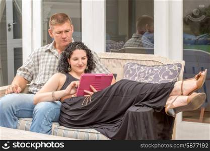 A young adult couple are together on the porch, viewing a digital device.