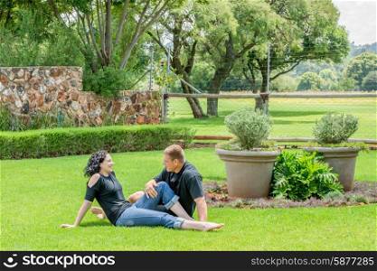 A young adult couple sitting outside their home on the lawn, talking to each other.